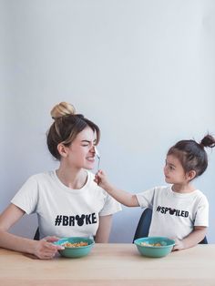 two women sitting at a table with bowls of food in front of them, one holding the other's hand