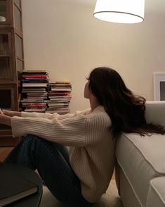 a woman sitting on a couch in front of a stack of books