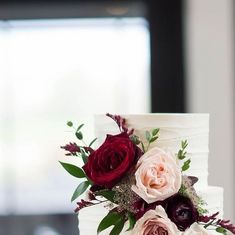 a three tiered white cake with red and pink flowers on it's side