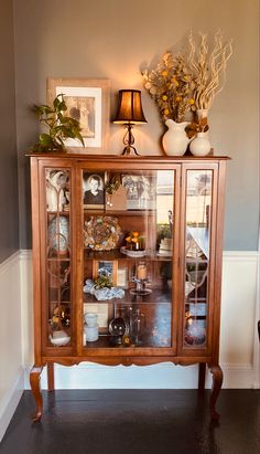 a wooden cabinet with glass doors and pictures on it's front door, next to a lamp