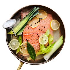 raw salmon with lemons, celery and onions in a frying pan