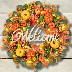 a wreath with the word welcome surrounded by autumn leaves and pumpkins on a white wooden background