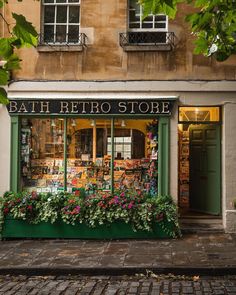 a store front with flowers in the window and on the sidewalk next to it is a green planter