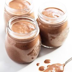 three jars filled with chocolate pudding on top of a white table next to a spoon