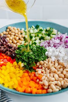 a bowl filled with beans, vegetables and dressing being poured into it