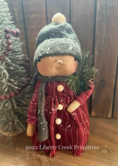 a small wooden doll standing next to a christmas tree with snow on it's head