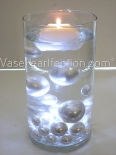 a candle that is inside of a glass with some balls in it and water on the bottom