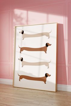 three dachshunds on a pink wall in front of a white frame with wood flooring