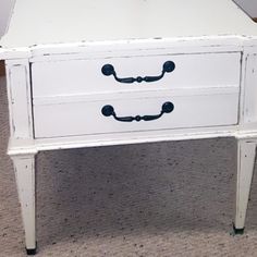 a white table with black handles and drawers on it's legs, sitting on carpeted floor