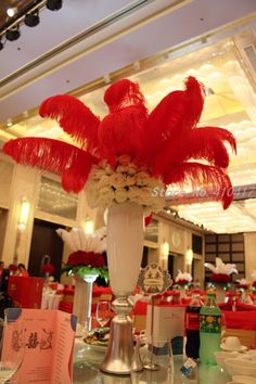 a vase filled with red feathers and flowers on top of a table in a restaurant