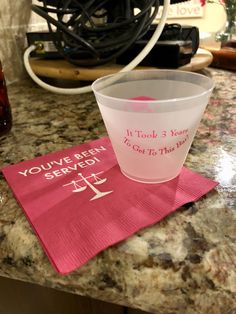 a plastic cup sitting on top of a counter next to a pink napkin that says you've been served get to this point