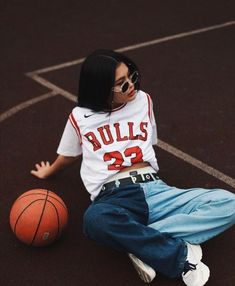 a woman sitting on the ground with a basketball in front of her and wearing sunglasses