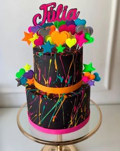 a black and pink birthday cake with colorful splatkles on the top tier