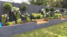 an outdoor garden with flowers and plants growing on the side of a fenced in area