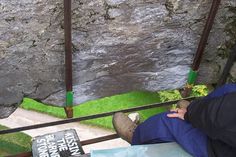 a man sitting on top of a metal bench next to a stone wall and green grass