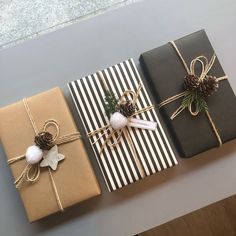 three wrapped presents sitting on top of a table next to pine cones and twine