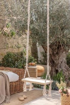 a white bench sitting under a tree next to a wicker basket and an olive tree