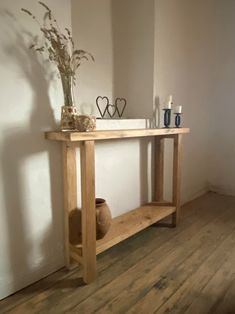 a wooden table with two vases on top of it next to a white wall