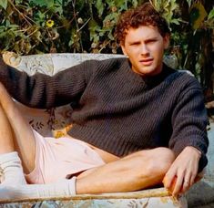 a young man sitting on top of a couch next to a plant filled with flowers