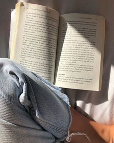 an open book sitting on top of a bed next to a person's leg