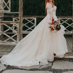 a woman in a wedding dress is standing on a porch with flowers and greenery