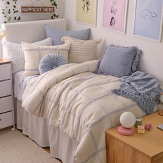 a bed with blue and white comforters in a bedroom next to a dresser, lamp and pictures on the wall