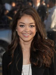 a woman with long brown hair smiles at the camera while standing in front of a crowd