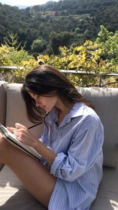 a woman sitting on top of a couch holding a pen and writing in a notebook