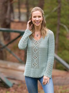 a woman is smiling and talking on her cell phone while wearing a crocheted sweater