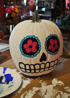 a white pumpkin decorated with red and blue flowers on it sitting on a table next to a paper plate