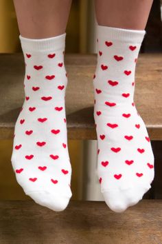 the legs of a person wearing white socks with red hearts on them, sitting on a wooden step