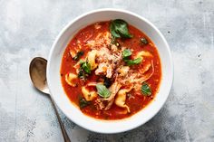 a bowl of pasta soup with spinach and meat in tomato sauce on a table