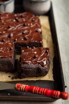 a chocolate cake on a tray with a knife next to it and two cups in the background