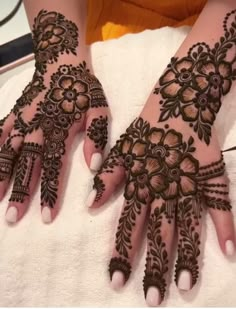 two hands with henna tattoos on them, one is showing off the intricate design