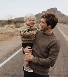 a man holding a little boy in his arms while standing on the side of an empty road