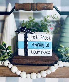 a gift wrapped in blue and white ribbon sitting on top of a wooden shelf next to green plants