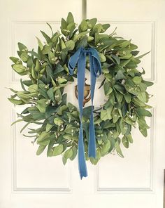 a wreath hanging on the front door with blue ribbon around it and a bell in the middle