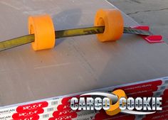 two orange skateboard wheels on top of a cardboard box with tape and scissors attached to them