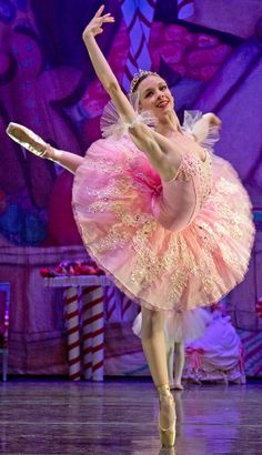 a ballerina in a pink tutu and white dress is dancing on stage with her arms outstretched