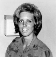 black and white photo of woman in uniform smiling at camera with box on wall behind her