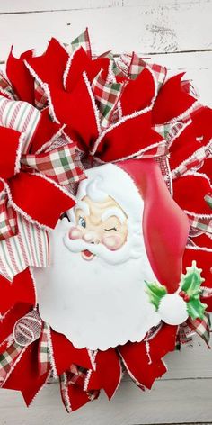 a christmas wreath with santa clause on it and red ribbon around the top, hanging on a white wooden wall