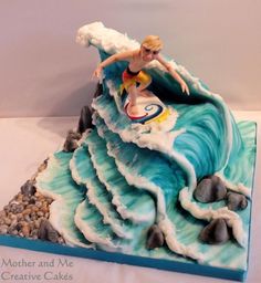 a cake made to look like a wave with a woman surfing on the top and rocks below