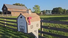 a mailbox in the shape of a barn sits on a fence near a farm