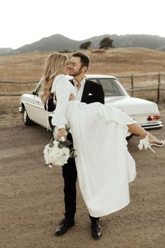 a newly married couple is posing in front of a car with their arms around each other