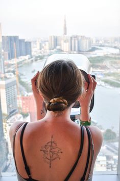 a woman with a compass tattoo on her back looking out at the city from a high rise building