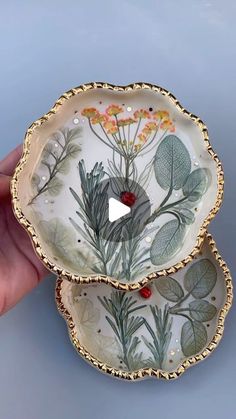 two plates with plants painted on them are held in the palm of someone's hand