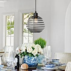 a dining room table with blue and white dishes on it, vases filled with flowers