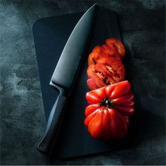 a knife and some sliced tomatoes on a cutting board with a black cloth next to it