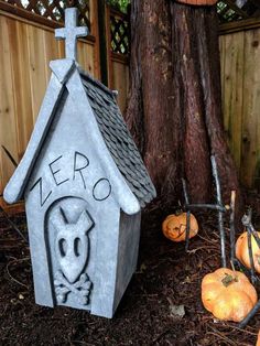 a cat house made out of cement next to pumpkins and a tree in the yard