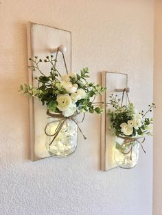 two mason jars with flowers are hanging on the wall